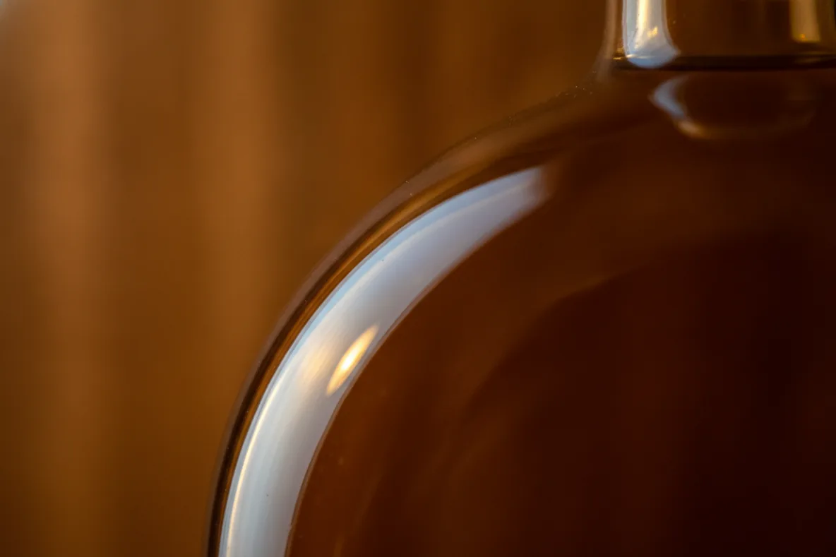 Makroaufnahme einer Glasflasche, über deren Schulter kühles und warmes Licht ineinander übergehen