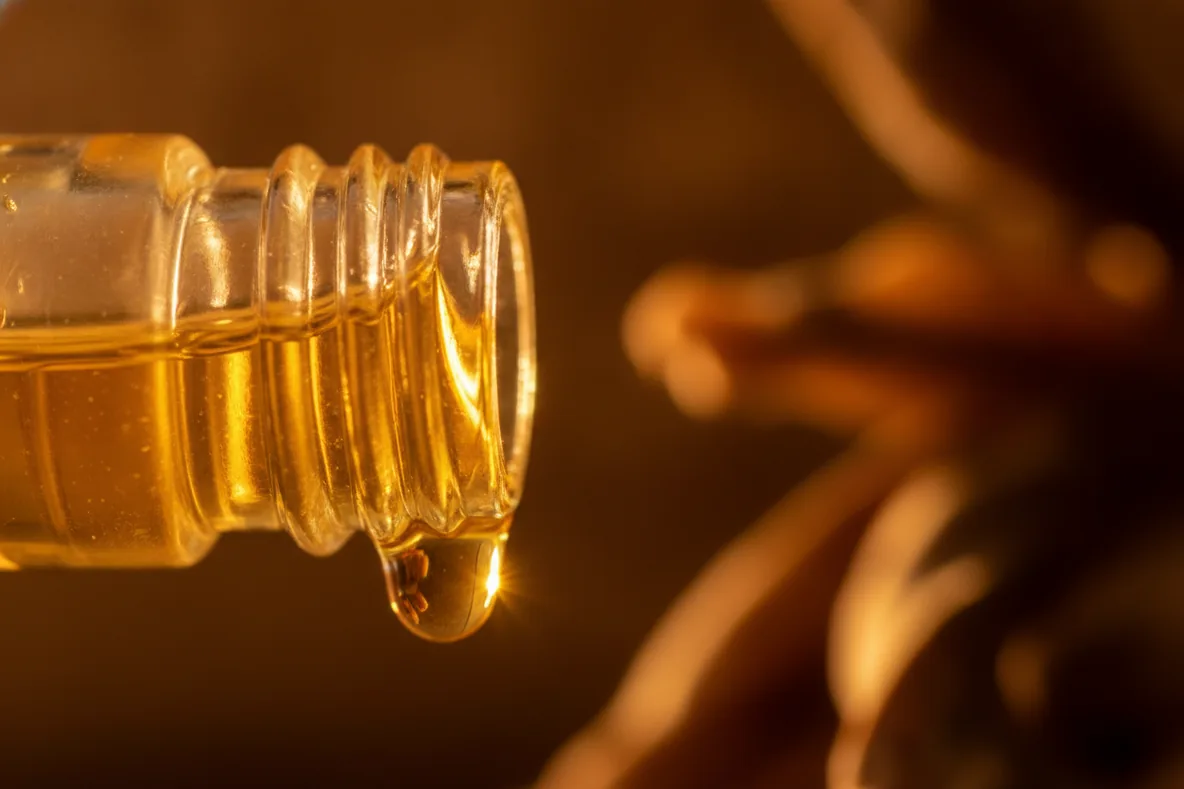 Makroaufnahme eines goldenen Öltropfens am Rand eines Glasfläschchens im Gegenlicht