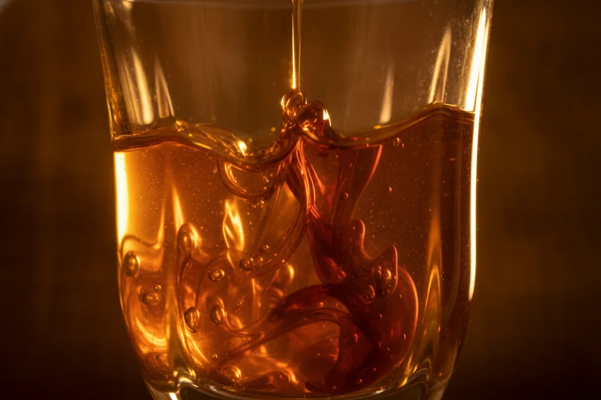 Makroaufnahme zweier Flüssigkeiten, die sich in einem Glas im Gegenlicht mischen